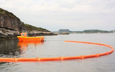 Orange arbeidsbåt legger ut blåser for å fange opp oljesøl